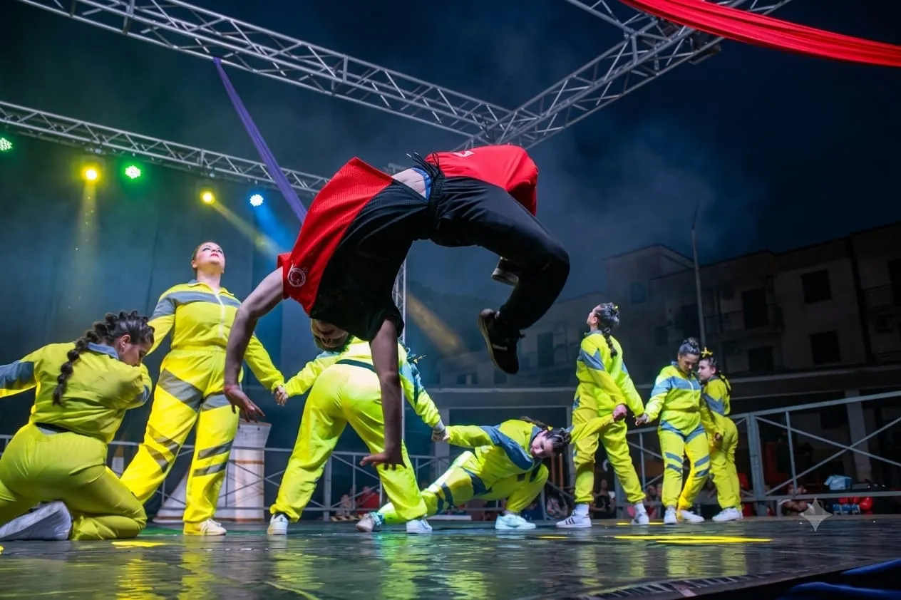 Gli allievi di Anima Danzante durante un'esibizione serale: un ballerino a mezz'aria in un salto acrobatico, il gruppo in tuta gialla intorno a lui